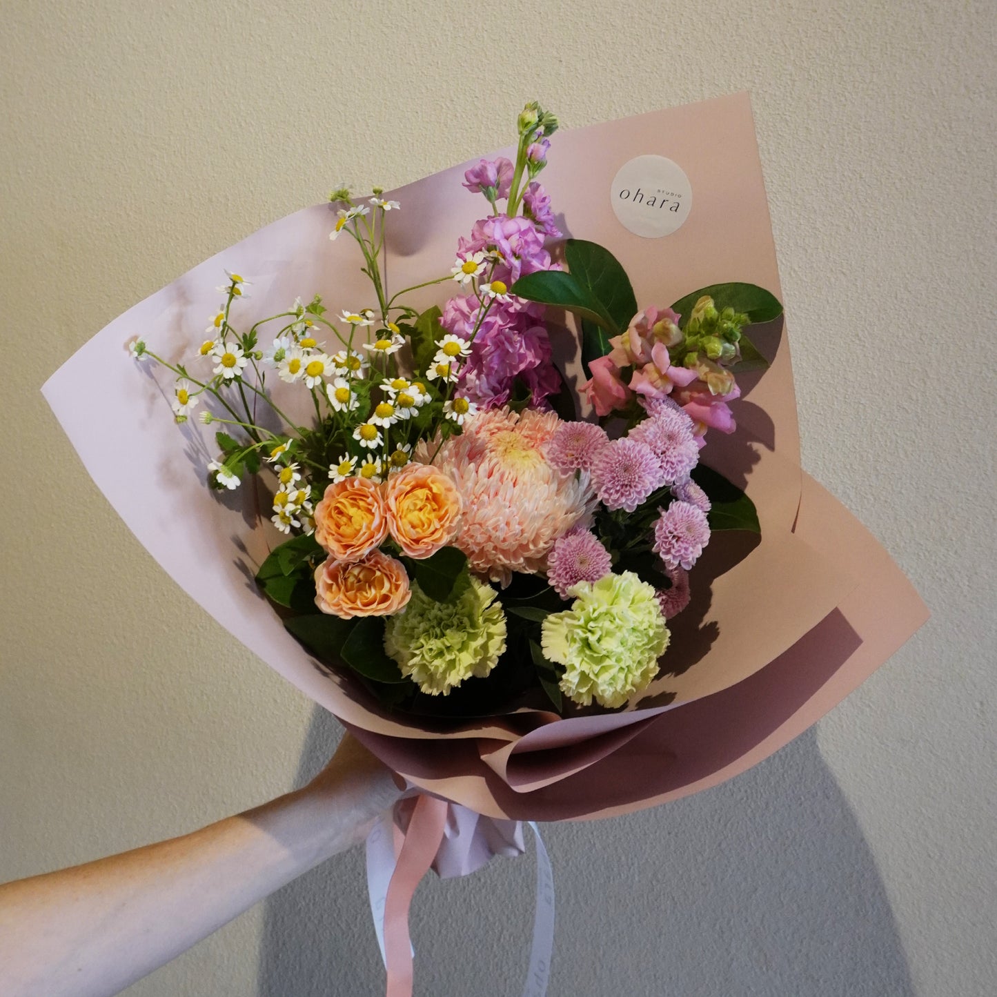 Bouquet of flowers wrapped in brown paper with a visible brand label, held against a plain background.