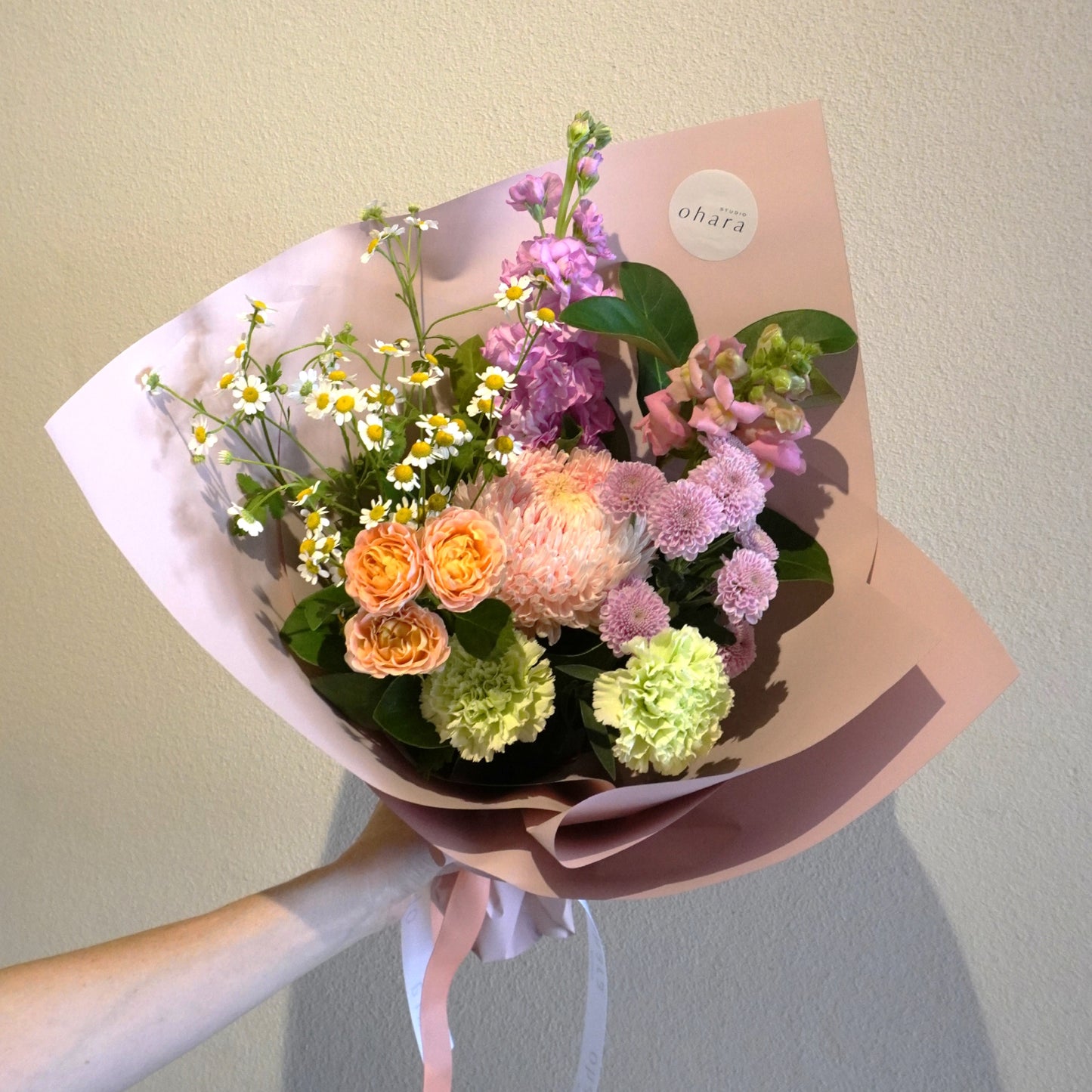 Bouquet of flowers wrapped in pink paper held by a person against a plain background