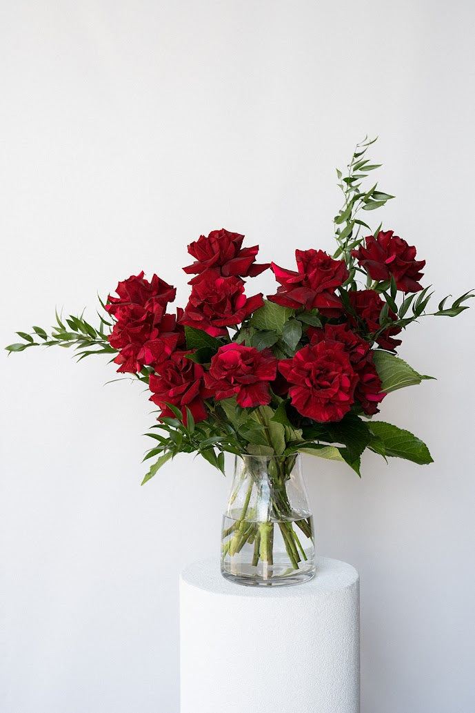 Bouquet of red roses in a clear vase on a white pedestal against a light gray background