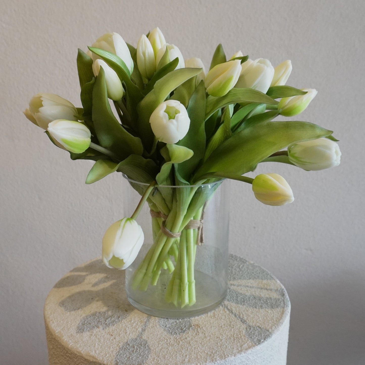 Clear glass vase with white tulips on a textured surface against a plain background