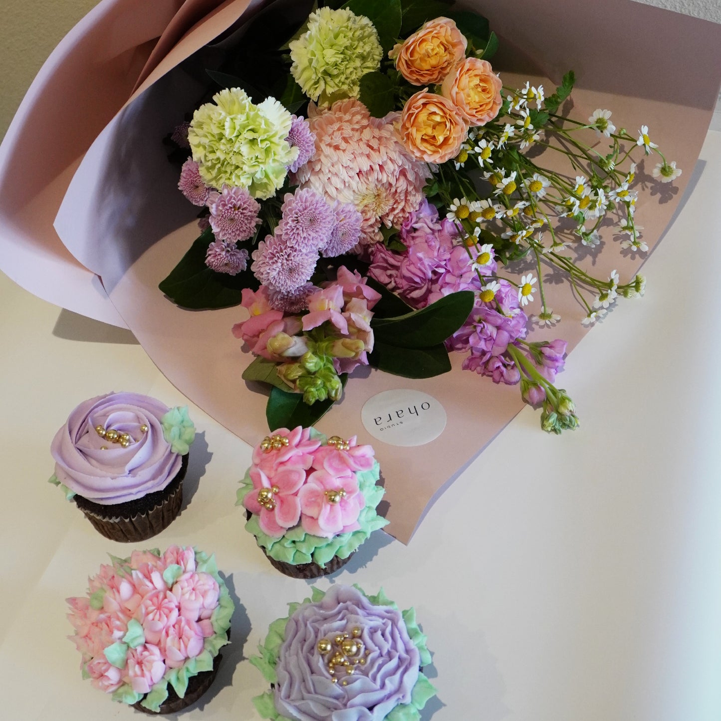 Bouquet of flowers with a pink box and decorated cupcakes on a light surface
