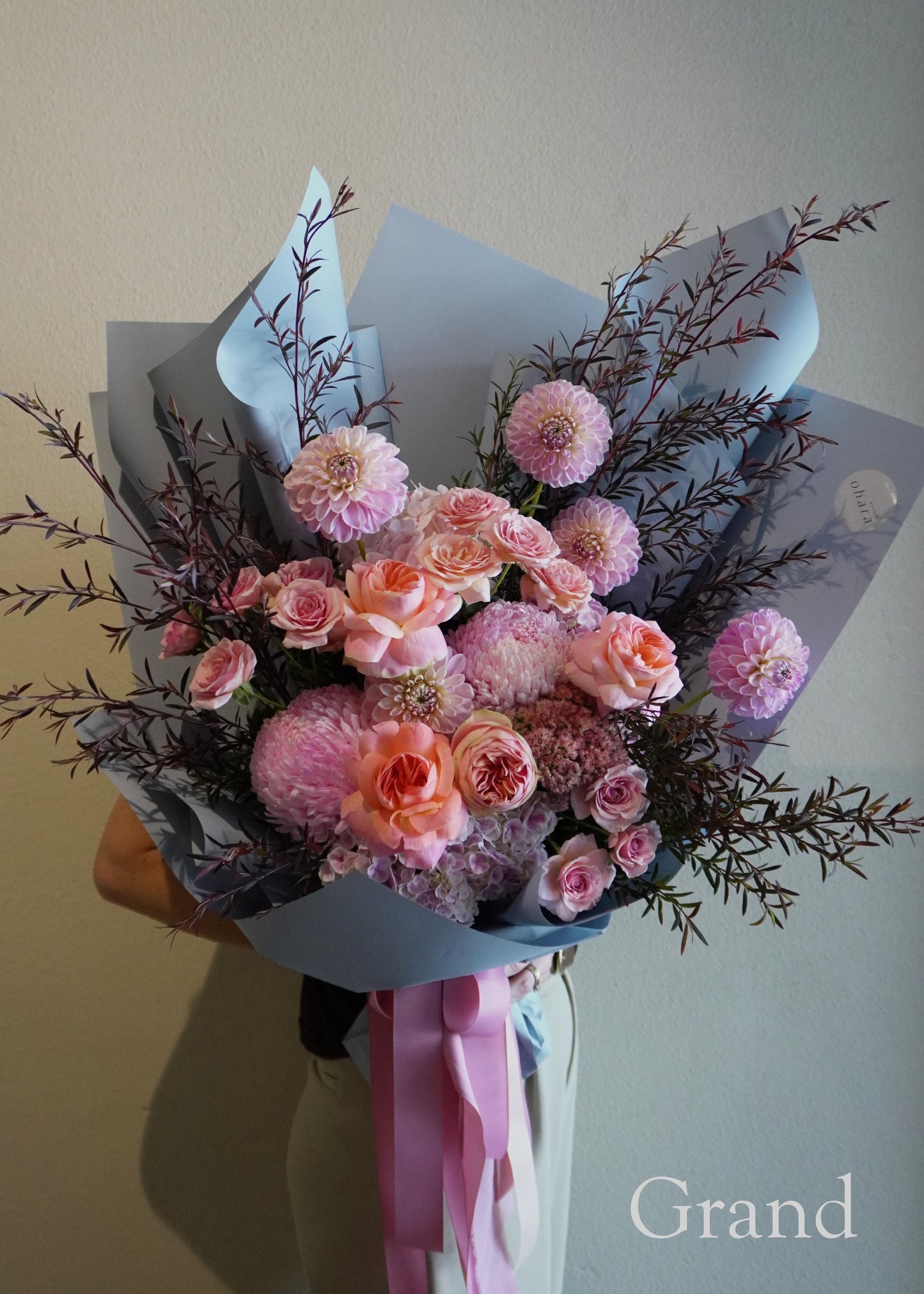 Bouquet of pink and peach flowers with a 'Grand' label on a neutral background