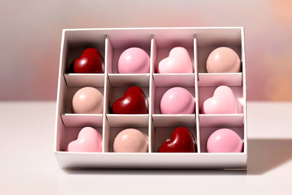 Box of heart-shaped chocolates in red, pink, and white on a light background