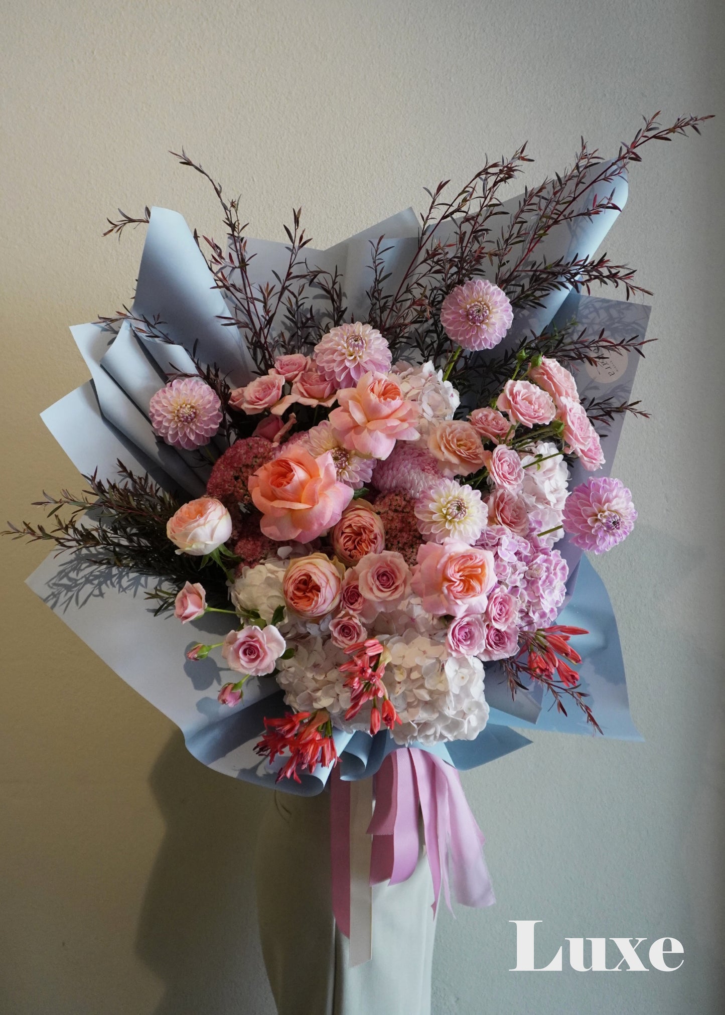 Bouquet of flowers with pink and white tones on a plain background, featuring the brand 'Luxe'.