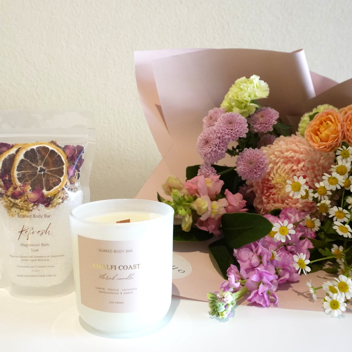 Candle and floral arrangement on a white surface with a neutral background