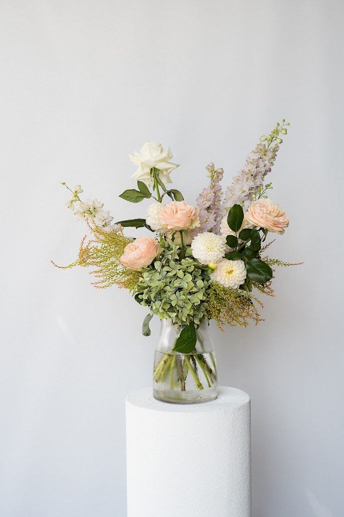 Bouquet of flowers in a clear vase on a white pedestal against a light gray background