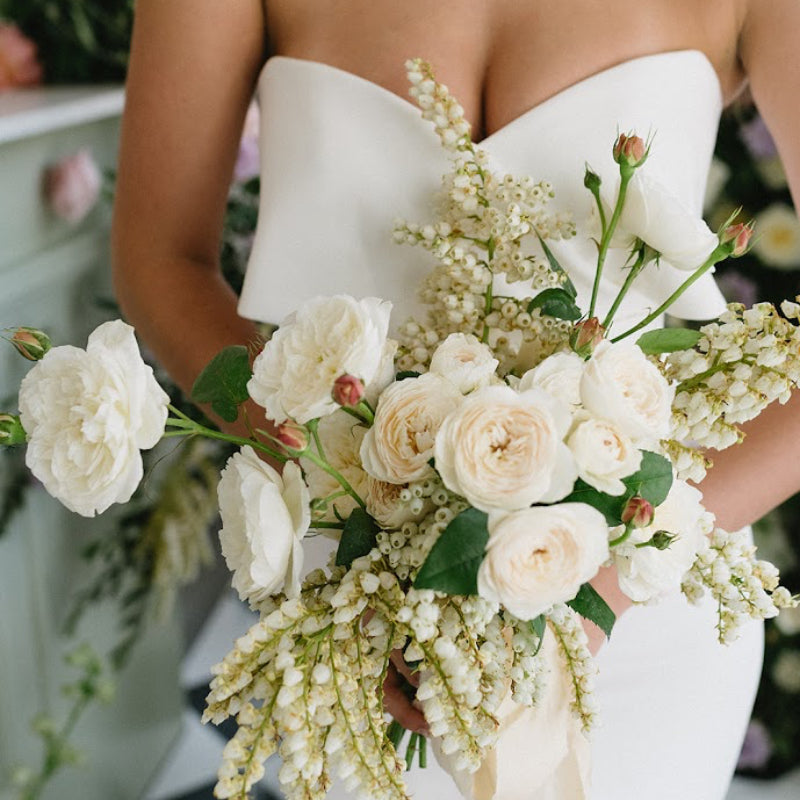 Bouquet of white and beige flowers held by a person wearing a strapless white dress.