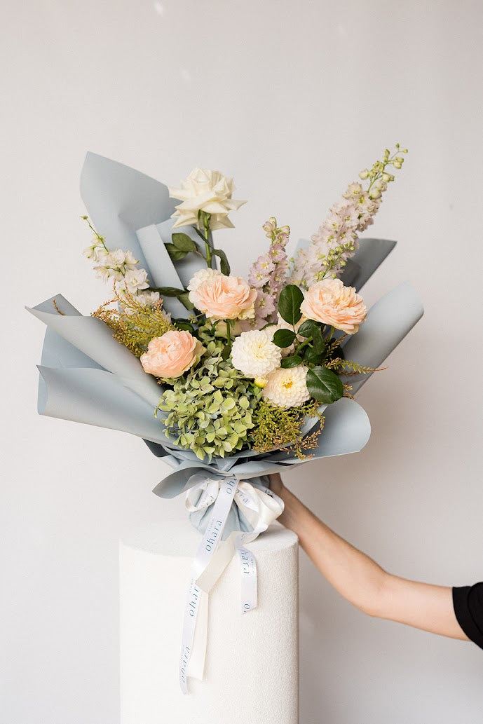 Bouquet of flowers with a gray wrap held by a person against a light background