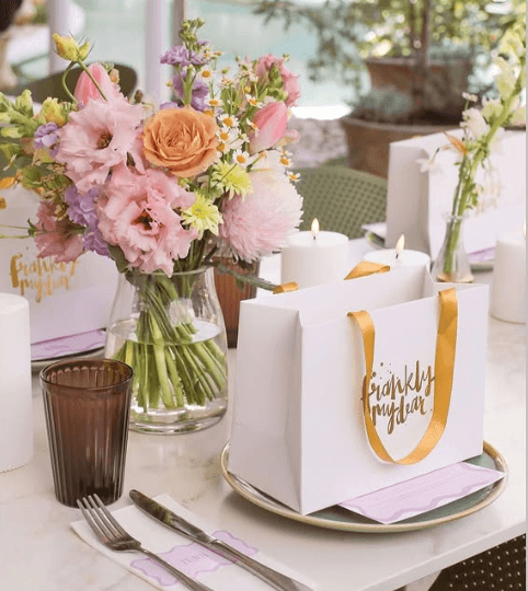 Decorative table setting with flowers, candles, and a gift bag on a table.