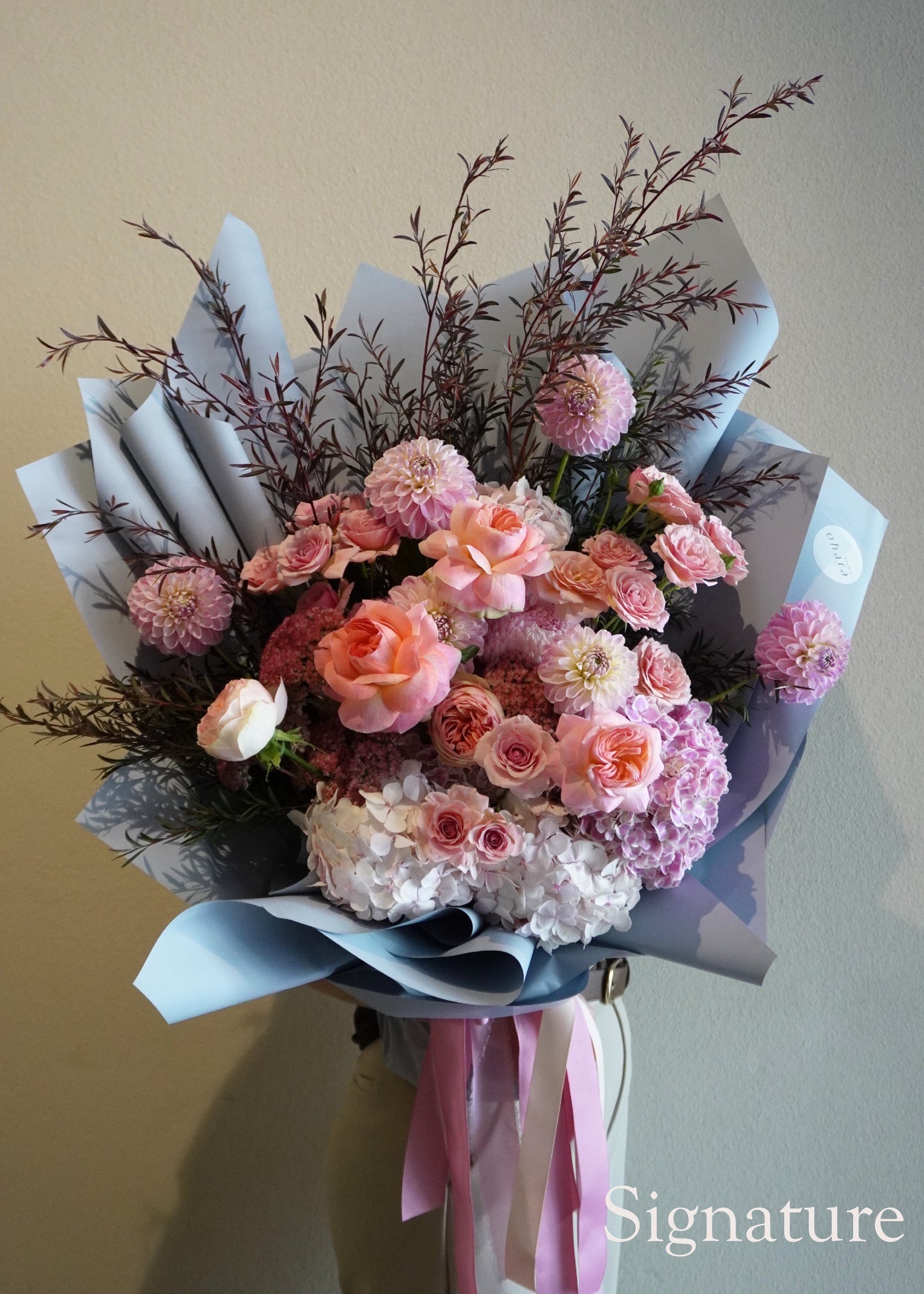 Bouquet of flowers with pink and white tones on a plain background, featuring the brand 'Signature'.
