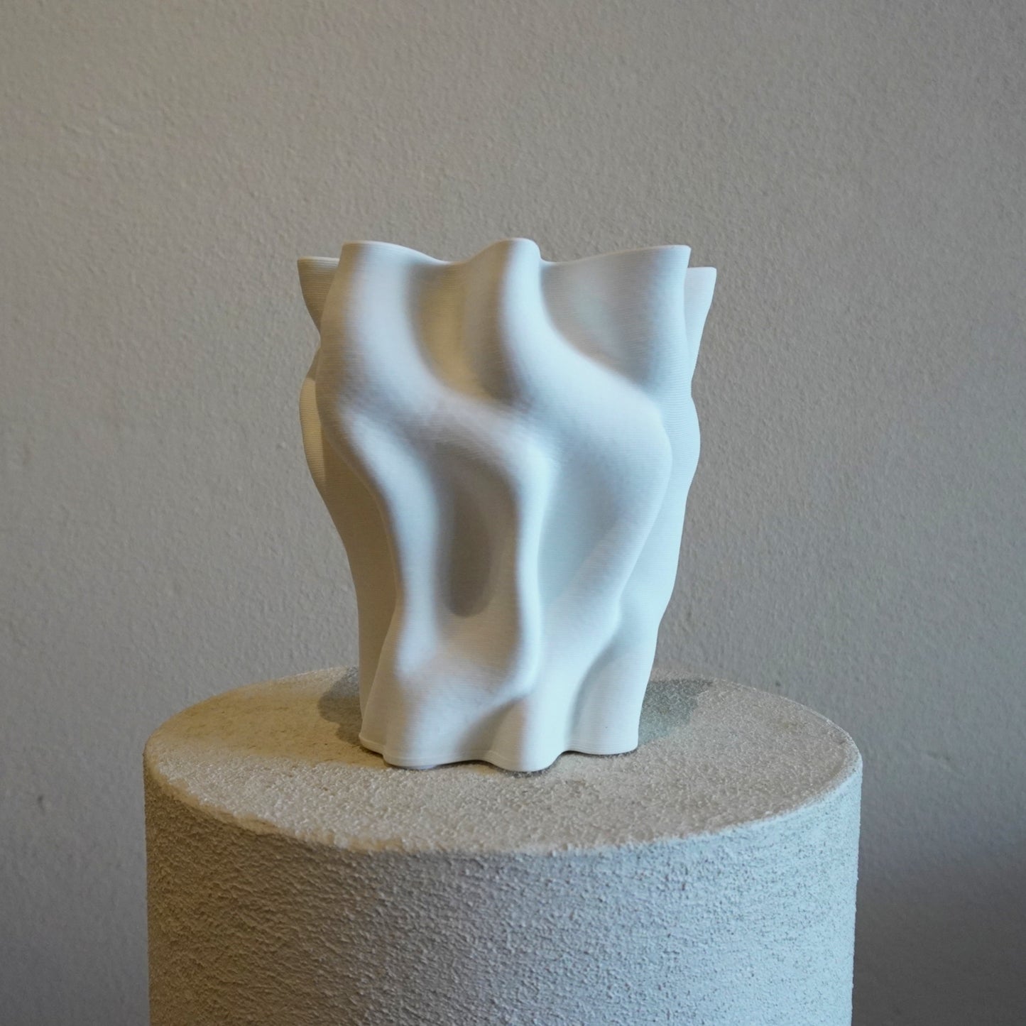 White abstract sculpture on a cylindrical pedestal against a plain background