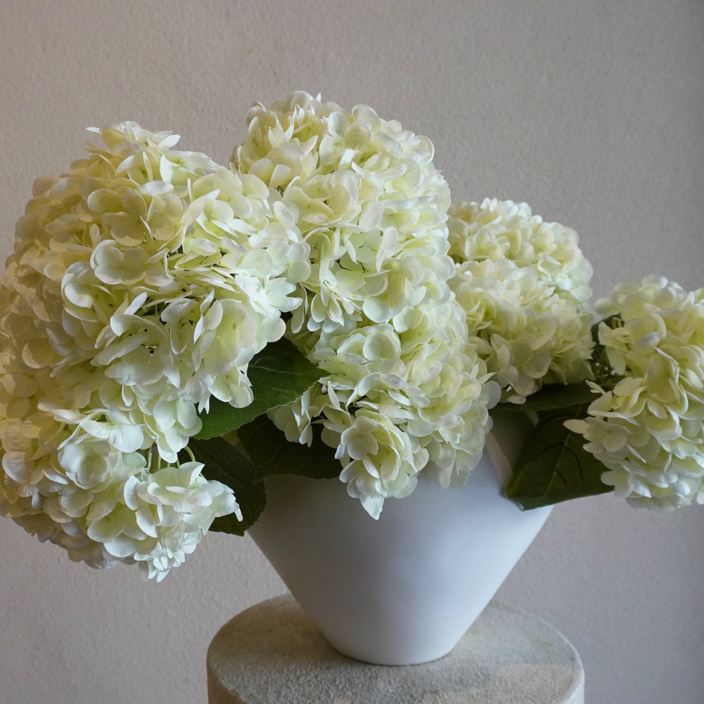 White hydrangeas in a white vase on a light surface with a neutral background