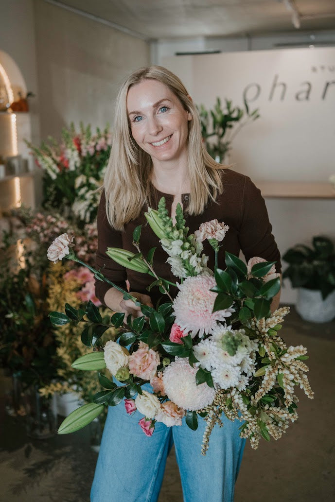 Woman holding a large floral arrangement in a flower shop setting