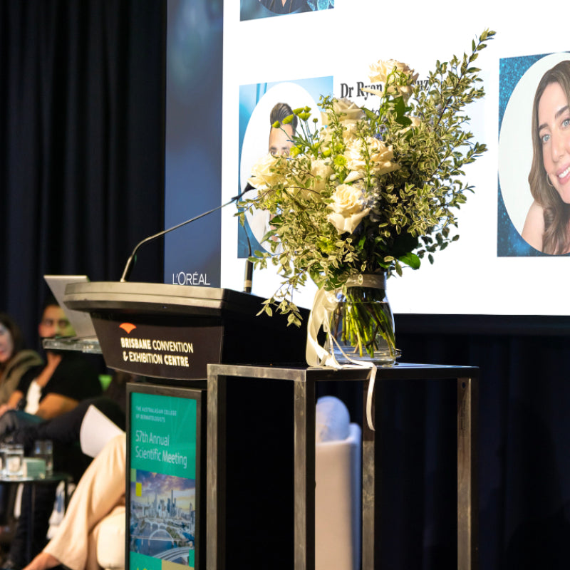 Podium with a vase of flowers and a screen displaying images in a conference setting.