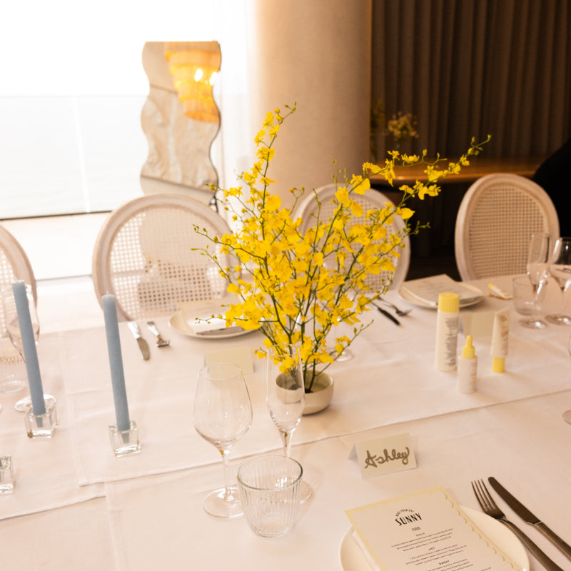 Elegant dining table setting with yellow floral arrangement, candles, and name cards.