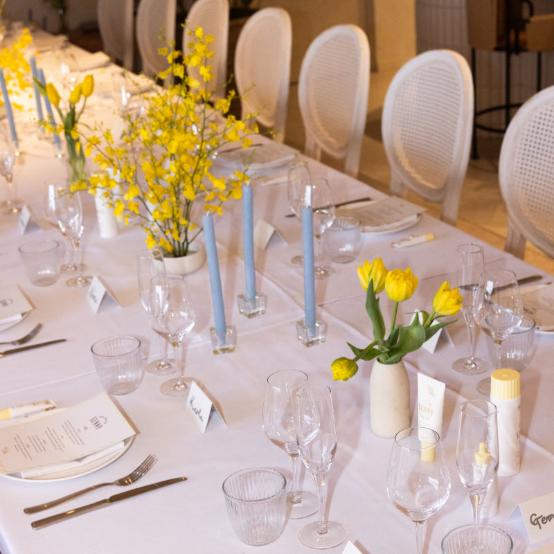 Elegant dining table setting with yellow flowers, blue candles, and white chairs.