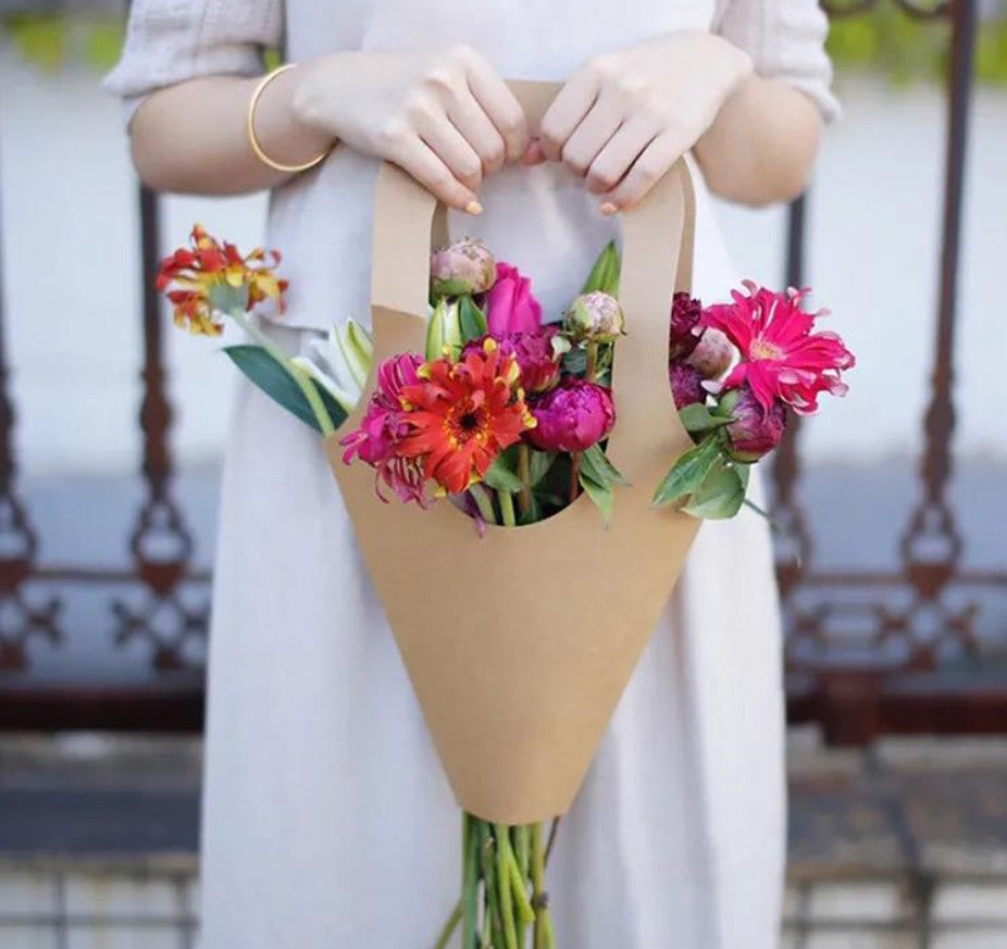 Bouquet of colorful flowers wrapped in brown paper held by a person.