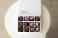Box of assorted chocolates with 'little cocoa' branding on a white stand.