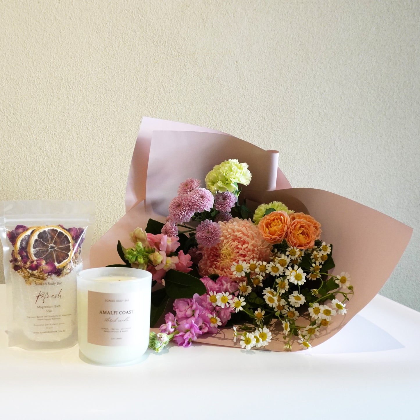 Bouquet of flowers with a candle and a bag of dried fruit on a white surface.
