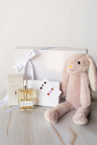 Pink plush bunny toy with a bottle of perfume and stationery items on a marble surface.