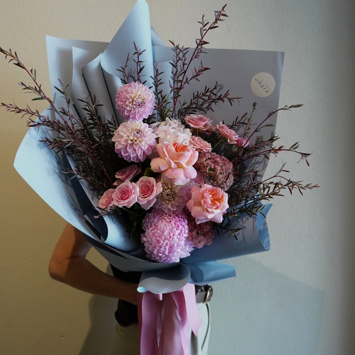 Bouquet of pink and purple flowers with a white paper wrap held by a person.