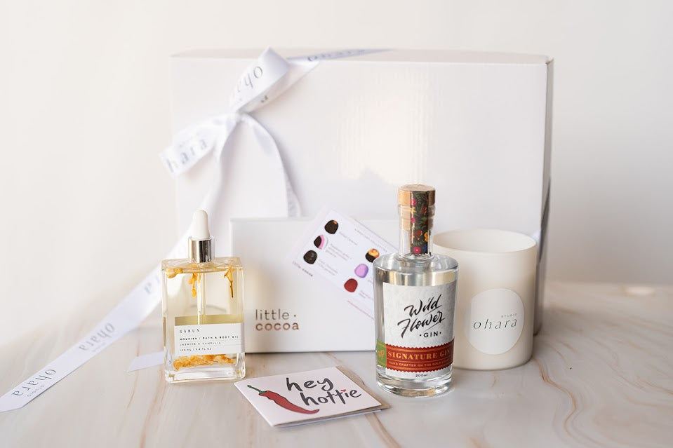 Two bottles of Wild Flowers and Co. products on a white surface with a white box and candle in the background.