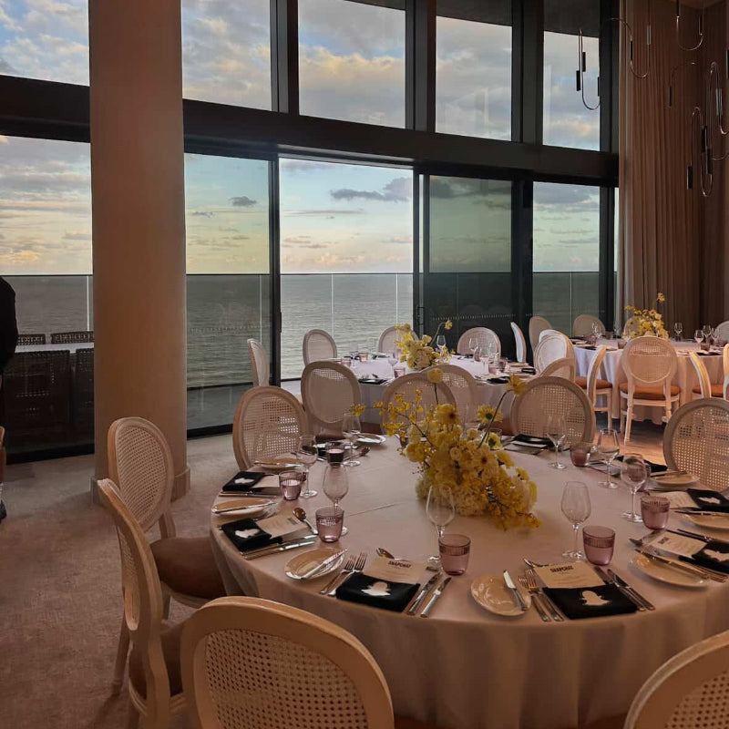 Dining area with tables set for a meal in a room with large windows overlooking water.