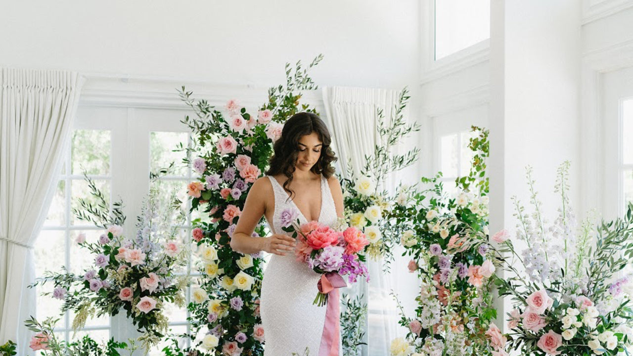 Woman in a white dress holding a bouquet of flowers in a room with floral decorations.
